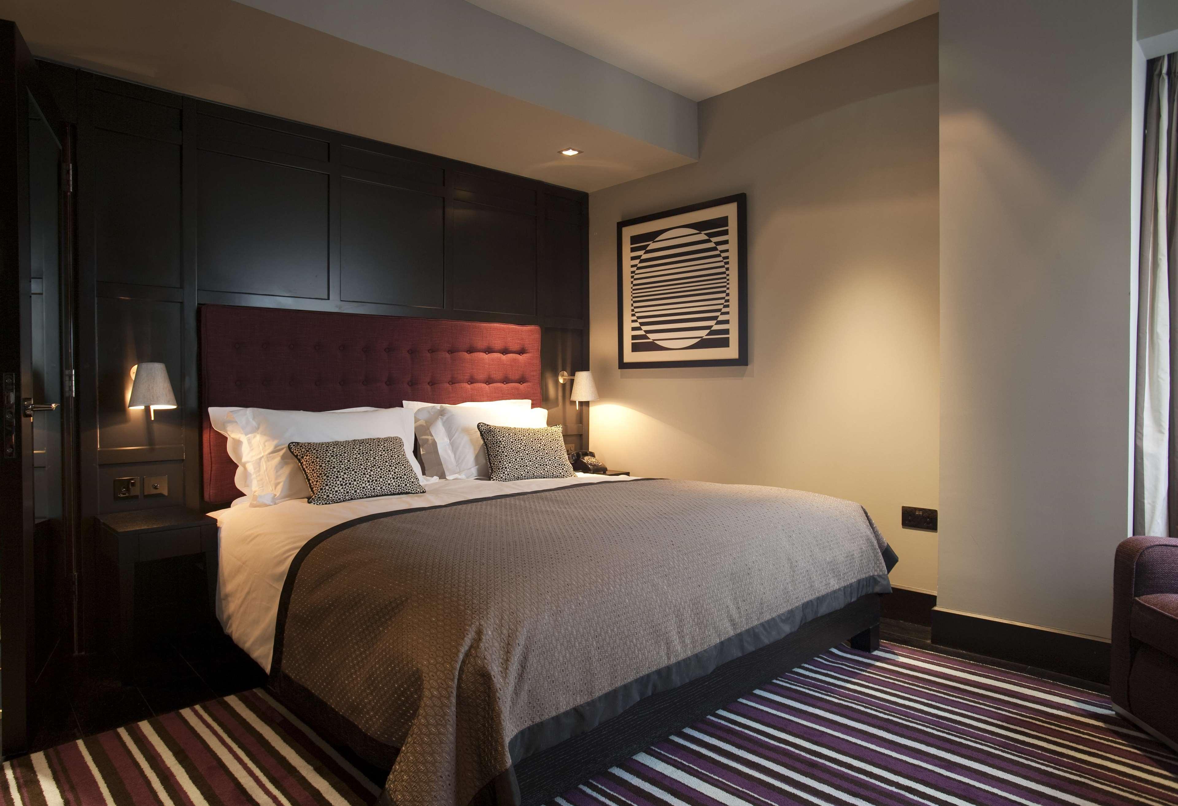 The Fitzwilliam Hotel Belfast Exterior foto The photo shows a stylish and modern hotel room. It features a large bed with a tufted headboard in a deep burgundy color. The bed is dressed with neutral-toned bedding and decorative pillows. On either side of the bed, there are small bedside lamps 