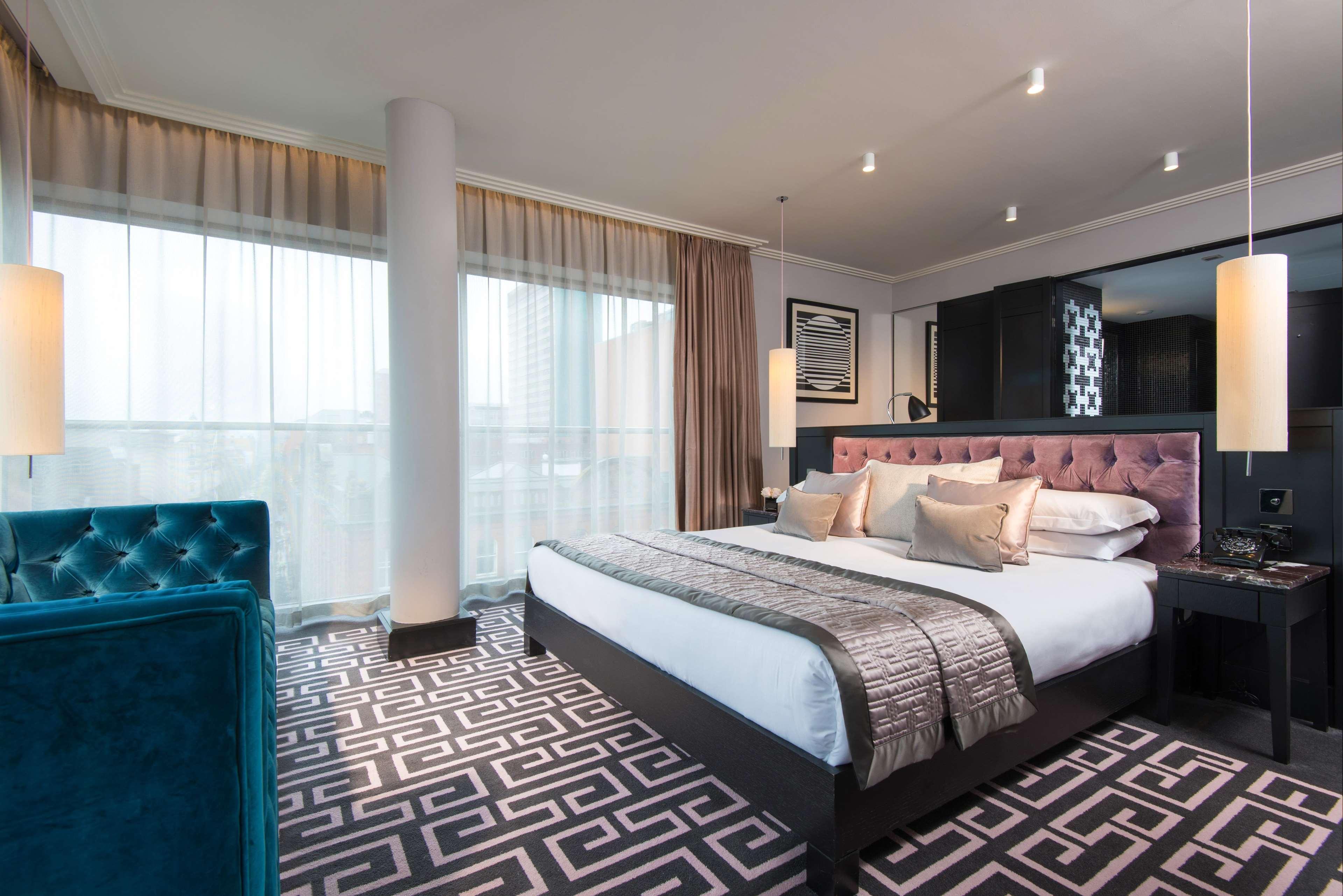 The Fitzwilliam Hotel Belfast Exterior foto The photo showcases a modern hotel room. It features a large bed with plush pillows and a stylish headboard. The room has large windows with sheer curtains, allowing natural light to filter in. The floor is covered with a patterned carpet that contra