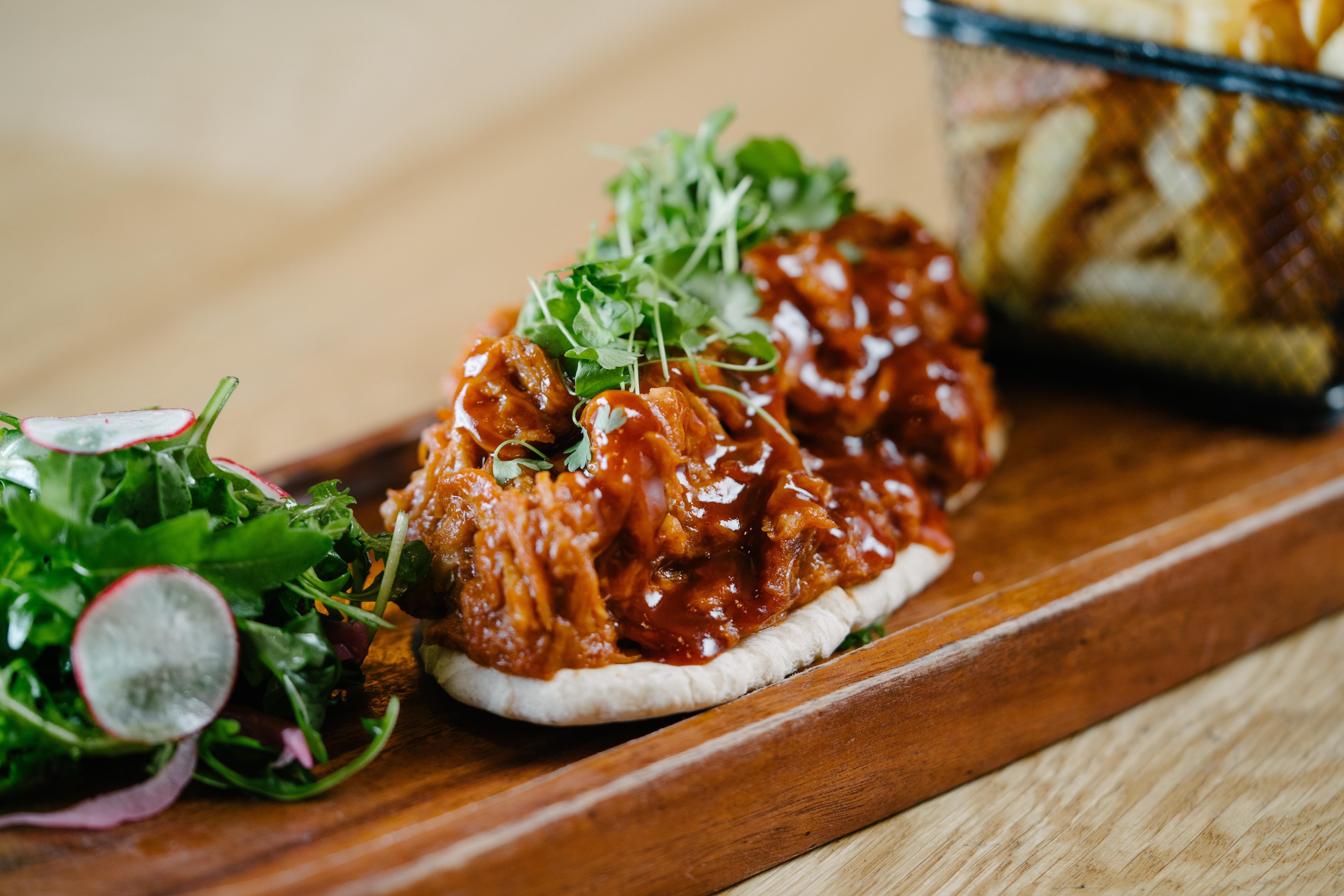 The Fitzwilliam Hotel Belfast Exterior foto The photo shows a wooden platter featuring two pieces of bread topped with pulled meat covered in a rich barbecue sauce. The dish is garnished with fresh greens, including sprouts. On the side, there is a small serving of mixed salad with radishes an